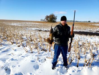 Portrait of man holding rifle and dead bird while standing on snow field