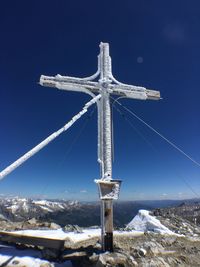 Cross on snow covered mountain against blue sky
