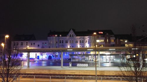 Railroad station by illuminated buildings in city against sky at night