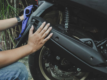 Midsection of woman cleaning motor scooter against plants