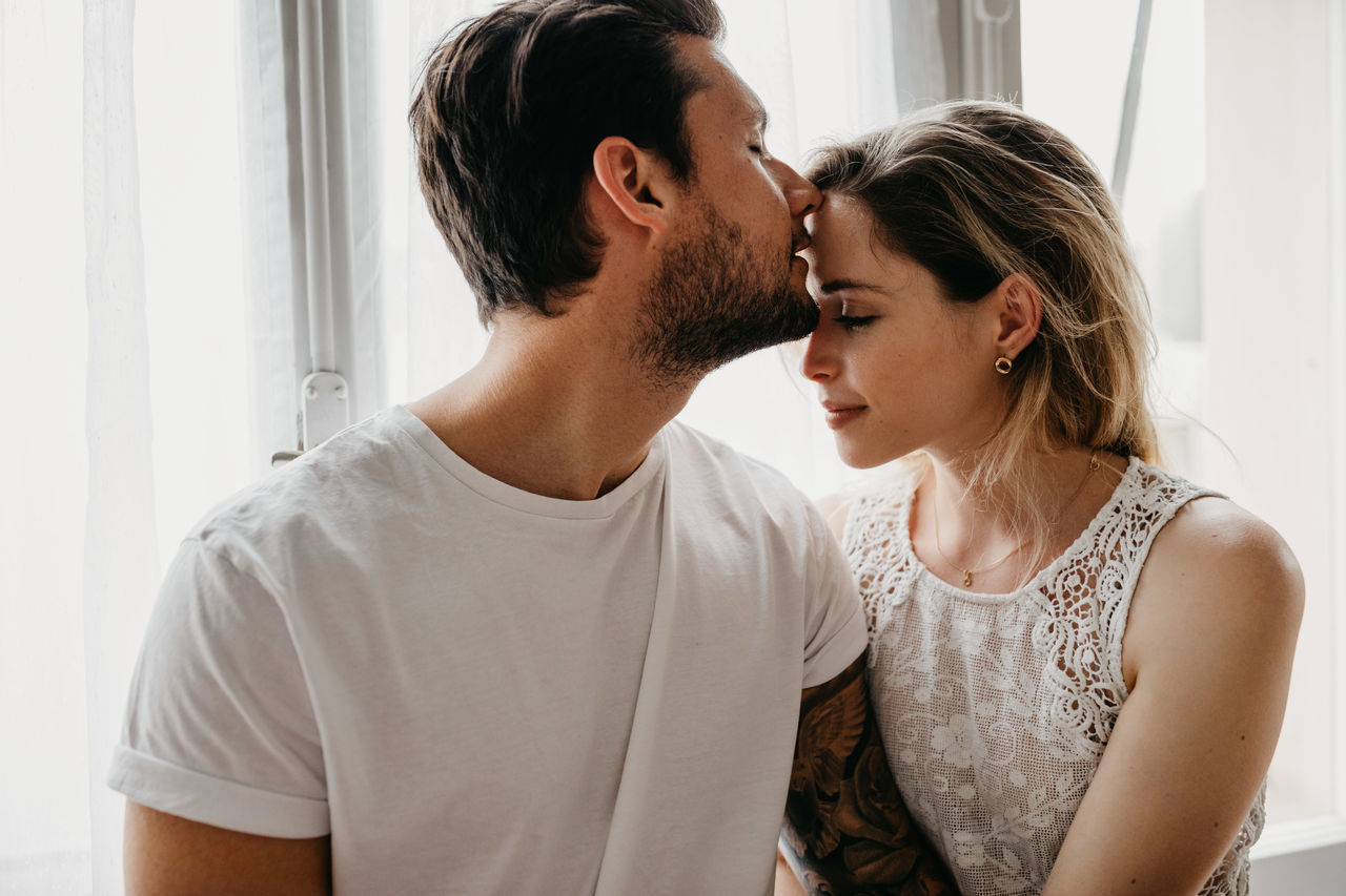 YOUNG COUPLE LOOKING AWAY WHILE SITTING ON FLOOR