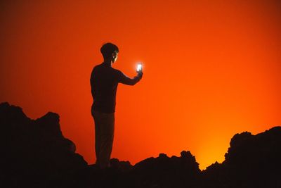 Silhouette of woman using smartphone against orange sky