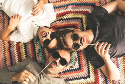 Portrait of father with sons holding prop mustache while lying on floor