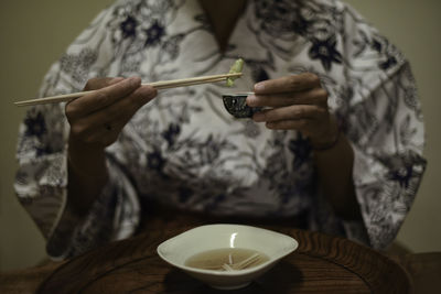 Close up view of hands of female caucasian woman in kimono using chopsticks to eat japanese food at ryokan