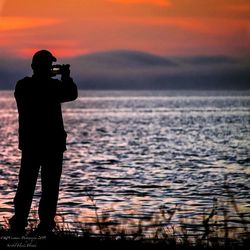 Silhouette of man standing in sea at sunset