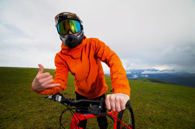 Serious professional cyclist in sportswear and helmet standing with a downhill bike on top of a hill