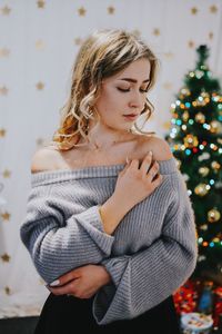 Young woman standing against christmas tree at home