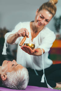 Smiling woman playing singing bowl for customer in spa