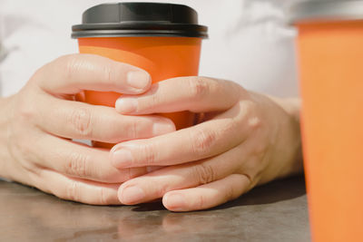 Close-up of the fingers and hands of a woman holding  bright orange glass of coffee during a break.
