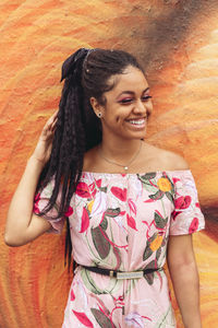 Young happy black lady in stylish clothes with afro braids looking away in the city