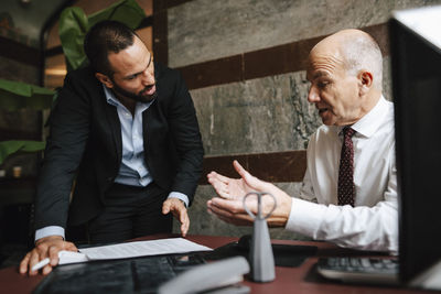 Senior male financial advisor discussing over contract with colleague at desk in office