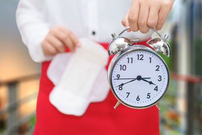 Midsection of woman holding alarm clock and sanitary pad