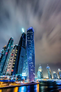 Low angle view of illuminated skyscrapers against cloudy sky