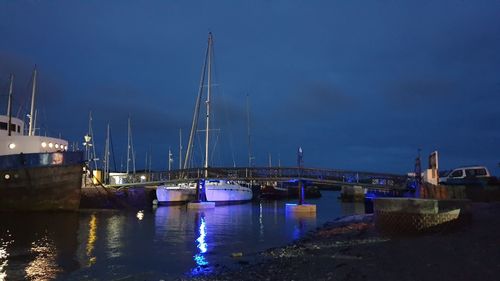 Sailboats moored in harbor against sky at night