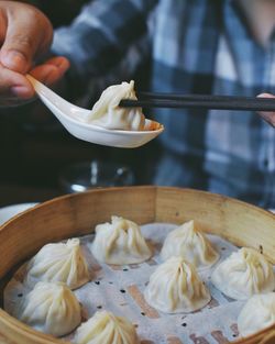 Cropped image of person holding dumpling with chopsticks in spoon