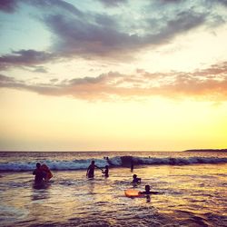 People on beach against sky during sunset