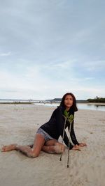 Full length of woman sitting on sand at beach against sky