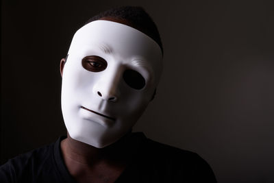 Close-up portrait of man wearing mask against black background