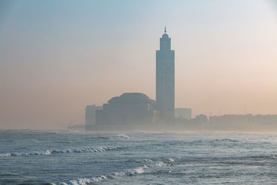 Lighthouse by sea against sky during sunset