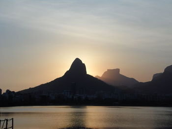Silhouette mountain by sea against sky during sunset