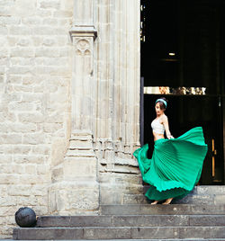 Beautiful woman holding skirt while standing on step by building