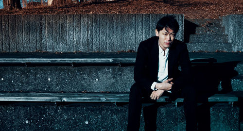 Sad man sitting on bench against wall