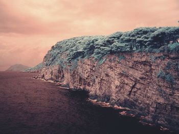 Cliff by sea against cloudy sky