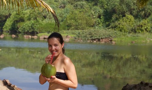 Portrait of smiling young woman drinking coconut water by lake at arambol