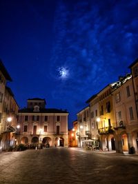 Illuminated street amidst buildings against sky at night