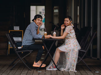 Portrait of couple holding hands sitting on chair at cafe