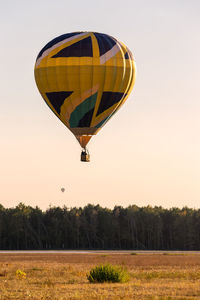 Hot air balloon flying over field against sky during sunset