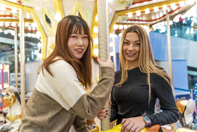 Millennial couple of multiethnic young women having fun after shopping on carousel