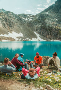 People sitting by lake against mountain range