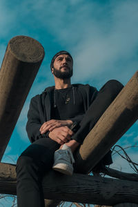 Man sitting on wood against sky