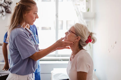 Mature female doctor examining patient's throat in medical examination room