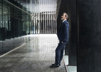 Mature businessman standing with hand in pocket leaning on black column