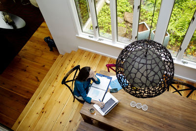 Overhead view of thoughtful woman using laptop while working on table at home