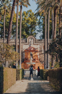 Rear view of people walking amidst trees against building