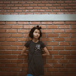 Cute girl looking away while standing against brick wall