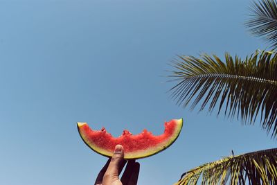 Low angle view of hand holding strawberry against blue sky