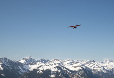 Low angle view of airplane flying over snow covered mountains against clear sky