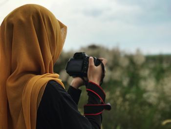 Close-up of woman holding camera while standing against sky