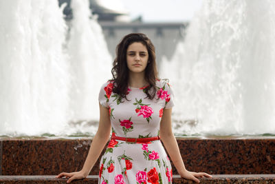 Portrait of beautiful young woman standing against fountain