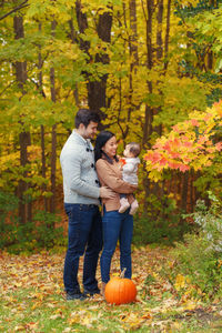 Parents playing with daughter while standing against trees during autumn