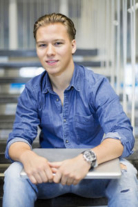 Portrait of confident student with laptop sitting on steps at university