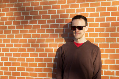 Young man wearing sunglasses while standing against brick wall