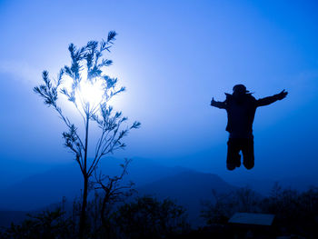 Silhouette man with arms outstretched against blue sky