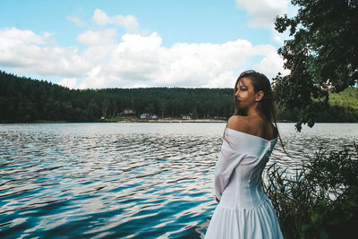 Young woman standing by tree against sky