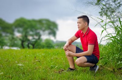 Thoughtful man crouching on grassy field