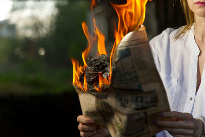 Midsection of woman holding burning paper outdoors